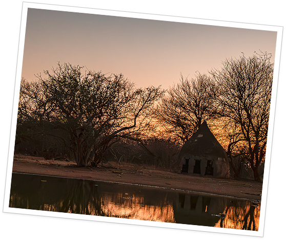 White-framed photograph of a safari camp reflected in water at sunset